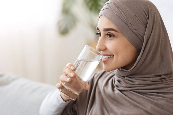 Perempuan berhijab tengah minum segelas air putih.(freepik)