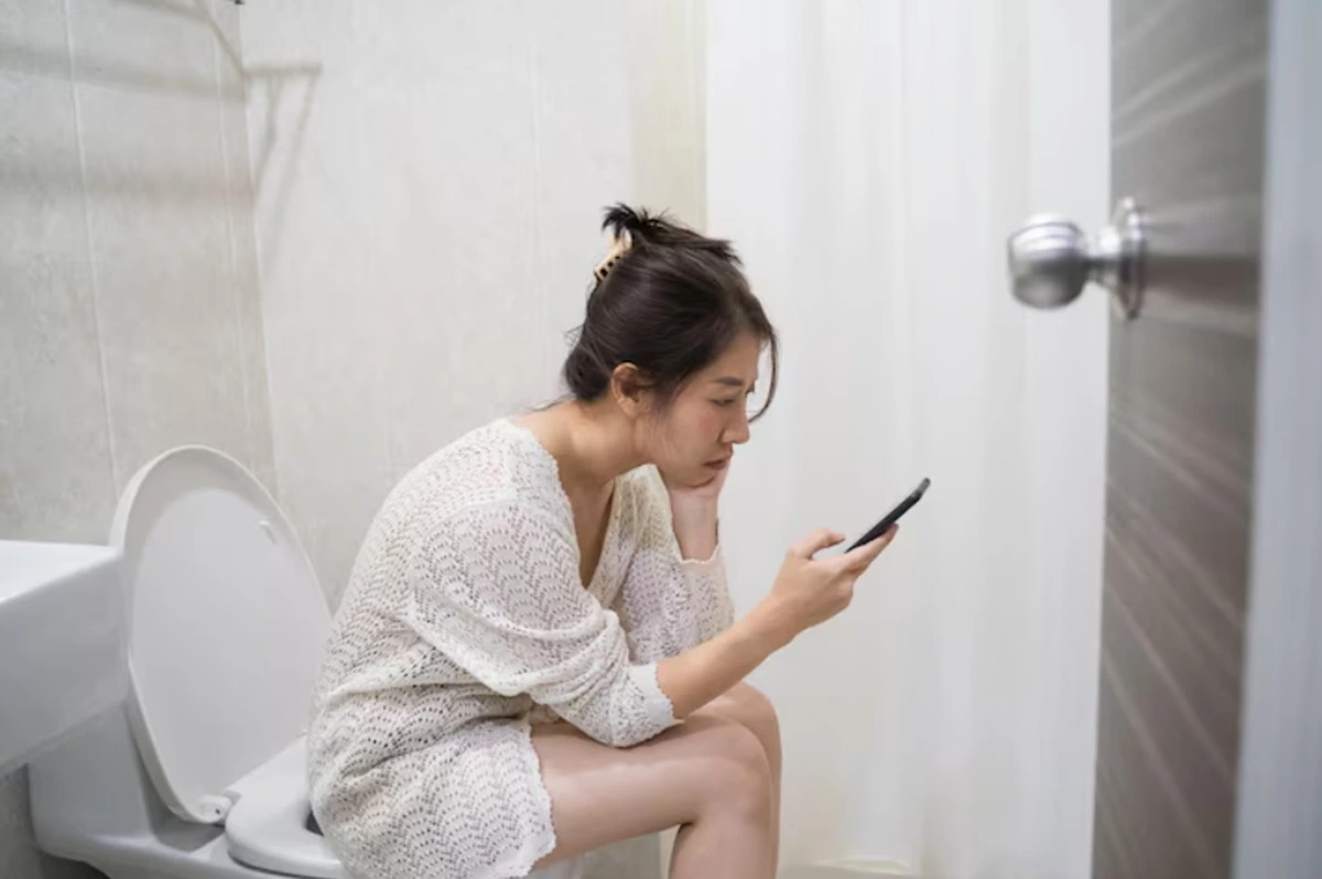 Seorang perempuan menggunakan ponsel di toilet.