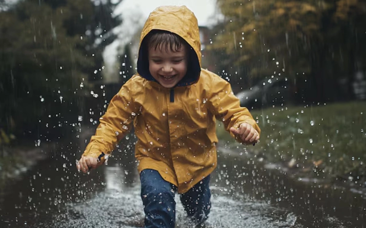 Seorang anak bermain hujan dengan bahagia.