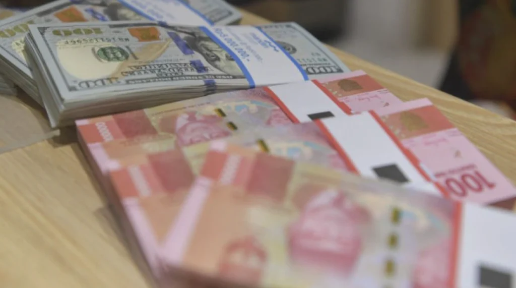 Teller bank tengah menghitung tumpukan Dolar AS dan Rupiah.(Antara)